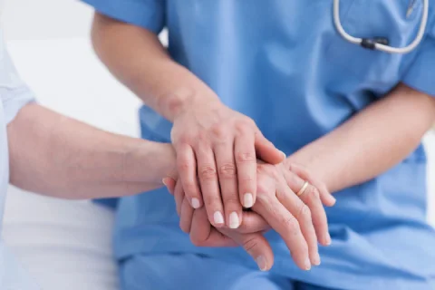 Two nurses holding hands in a hospital room.