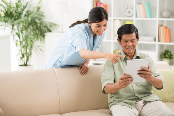 A woman is helping an older man use his tablet.